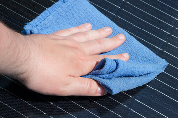Hand with a towel cleans the surface of solar panel. Remove the dust from electrical photovoltaic panels for better efficiency.