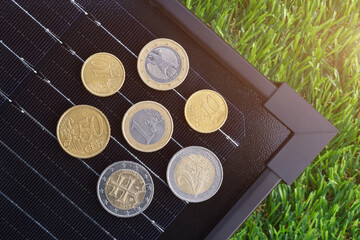 The concept of the solar energy generation cost in Europe. The euro coins on electrical solar panel placed on the green grass.