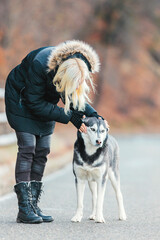 A woman with long brunette hair pets a majestic husky dog on the side of a deserted road, bonding through touch and affection