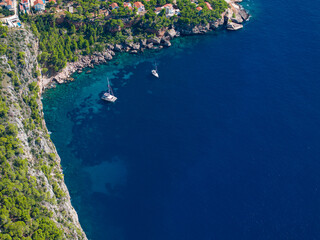 AERIAL: Flying above two sailboats anchored by the rugged coastline of Hvar.