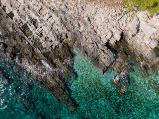 TOP DOWN: Unrecognizable female tourist sunbathes on the rocky beach in Croatia.