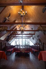 Wooden Lodge Interior with High Ceiling, Chandelier, Red Tables, Animal Heads