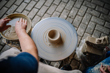Fototapeta premium Dobele, Latvia - August 18, 2023 - Overhead view of hands shaping clay on a spinning pottery wheel, with blocks of clay and tools on the side.