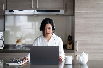 Young Asian professional woman working from home on her laptop while sipping a hot drink.