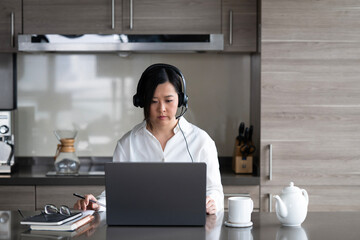 Young Asian professional woman working from home on her laptop while sipping a hot drink.