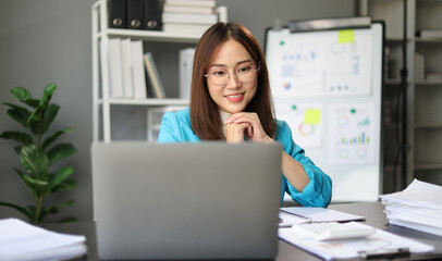 Asian businesswoman working on documents with laptop in office.