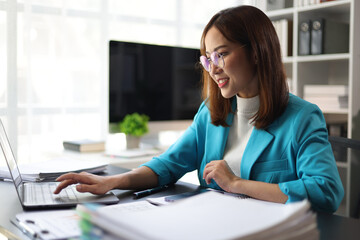 Asian businesswoman working on documents with laptop in office.