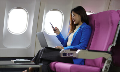 Businesswoman traveling on airplane working with laptop. Asian female tourist using laptop in aircraft, woman holding mobile device for playing game or working during flight.