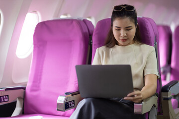 Businesswoman traveling on airplane working with laptop. Asian female tourist using laptop in aircraft, woman holding mobile device for playing game or working during flight.