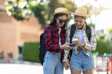 Two young Asian female tourist friends reading a tourist map on their mobile phone on the street in Thailand.