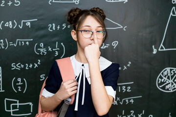 beautiful schoolgirl adjusts her glasses on her nose while standing at the school board.