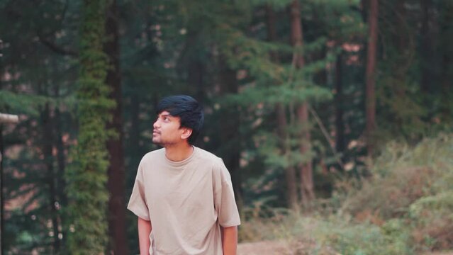 Portrait of an Indian male tourist walking in front of Pine tree forest at Manali in Himachal Pradesh, India. Tourist exploring Van Vihar national park in Manali. Man walks in front of pine tree