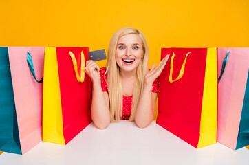 Photo portrait woman sitting at table bags showing credit card amazed isolated bright orange color background