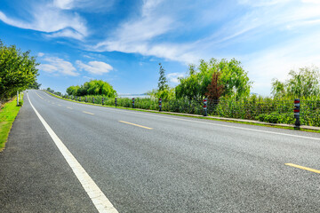 Countryside asphalt road and green trees with sky clouds on a sunny day