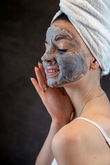 Beautiful young woman wear white towel applying gray oxygen bubbling mask isolated on black