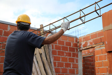 Builder lifting an iron column to make beams. Bricklayer with safety helmet and gloves working on a...