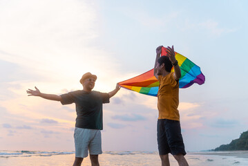 Happy Gay couple waving lgbt flag on sunset light in beautiful beach. Happy guys demonstrate their...