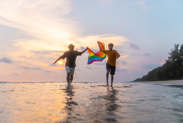 Happy Gay couple with lgbt flag running together on the beach in summer day. Happy guys demonstrate their rights. LGBTQI, Pride Event, LGBT Pride Month, Gay Pride Symbol.