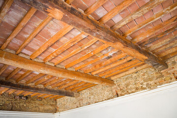 Old traditional italian wooden ceiling with damaged wooden beams, rafters and terracotta tiles clay bricks in italian language called mezzane - Tuscany culture - Italy