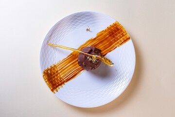 Single round chocolate cake with gold leaf on white plate with brown sauce