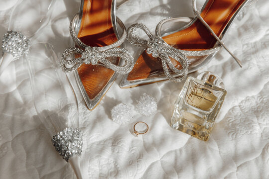 A pair of silver shoes with a bow on the front and a bottle of perfume next to them