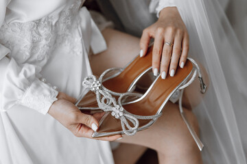 Fototapeta premium A woman is holding a pair of high heels with a bow on them. The shoes are silver and sparkly, and the woman is wearing a white dress. Concept of elegance and sophistication