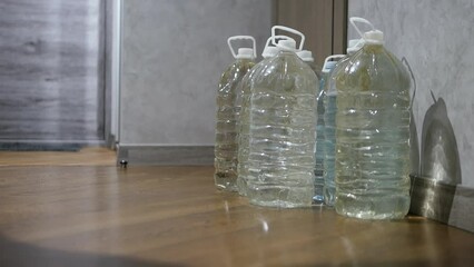 A man stores drinking water in plastic bottles. Drinking water shortage. Storing bottled water at home. - Powered by Adobe