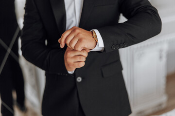 A man in a suit is wearing a gold watch and adjusting his cuff. Concept of formality and attention...