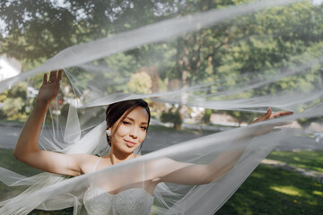 A woman in a white dress is standing in front of a tree with a veil over her head