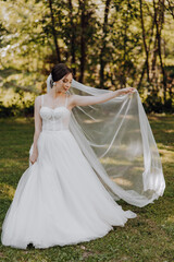 A bride is standing in a field with a white veil and a white dress. She is holding a white scarf in her hand