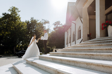 A bride and groom are walking up the steps of a building. The bride is wearing a white dress and...