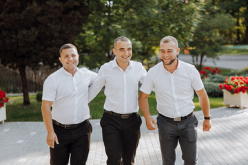 Three men in white shirts and black pants are walking together. They are smiling and seem to be...
