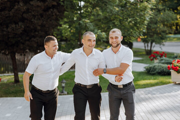 Three men in white shirts and black pants are standing together and shaking hands. Scene is...