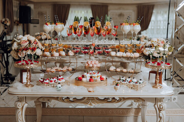 A table with a variety of desserts and drinks, including fruit and wine glasses. The table is set...