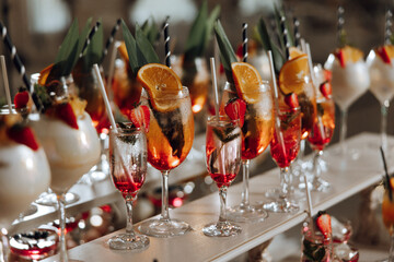 A table full of drinks with a variety of fruit garnishes and straws. The drinks are in tall glasses and the table is white