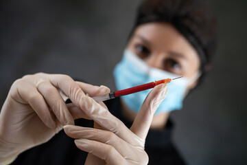 woman doctor in black uniform mask and gloves holding blood sample  in syringe isolated on dark