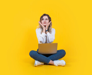 Full body size caucasian blonde woman with curly hair full body size sitting yellow studio background with laptop looking aside copy space hold face with hands astonished. Lifestyle concept.