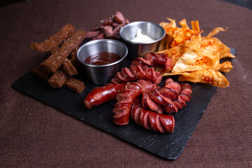 Top view of a plate of food with bread, meat, sausage, and chips with dip.
