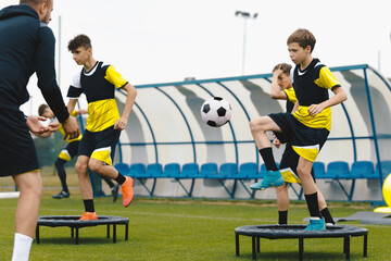 Group of young boys in sports soccer club practicing on jumping trampoline. Teenagers on football training trampoline. Youth athletes improving stability skills with young coach. Boys agility practice