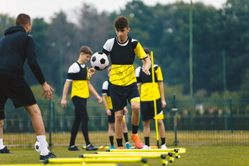 Player kick soccer ball to coach and ladder skipping. Teenagers on soccer training camp. Boys practice football with young coaches. Junior level athletes improving soccer skills on outdoor training