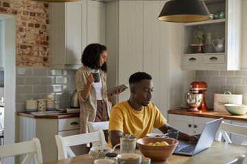 Young multiethnic couple doing different things during breakfast at home