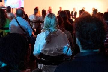Background of unrecognizable people standing with their backs to the camera and facing the stage where the speakers are speaking. Business event. High quality photo