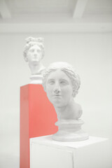 White sculptures of female heads on podiums against gray background.