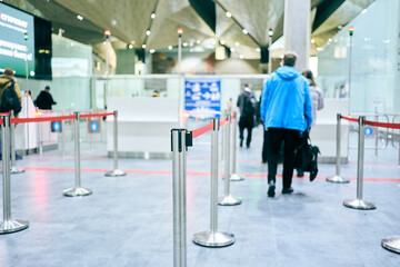 A red retractable barrier at the airport check-in desk. People are lining up to register. Copy...