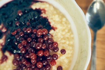 A close-up of a plate of wheat porridge for a healthy gluten-free breakfast. Warm wheat porridge with red currants and blueberry jam. High quality photo
