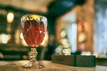 A filled wine glass with a traditional multifaceted shape, on a wooden bar counter with a blurred...