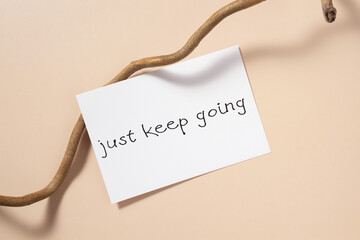 White paper blank, tree branch on beige background. Motivation quote card on beige table. Just keep going