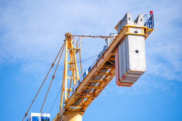 Tower Crane Against Blue Sky: Close-up view of a towering yellow crane with a heavy concrete counterweight under a clear blue sky