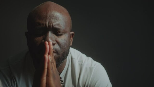 Hopeful African American man holding hands together and praying deeply to God with eyes closed