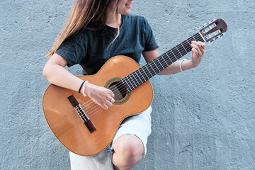 photograph of an unrecognizable woman playing an acoustic guitar on a neutral background